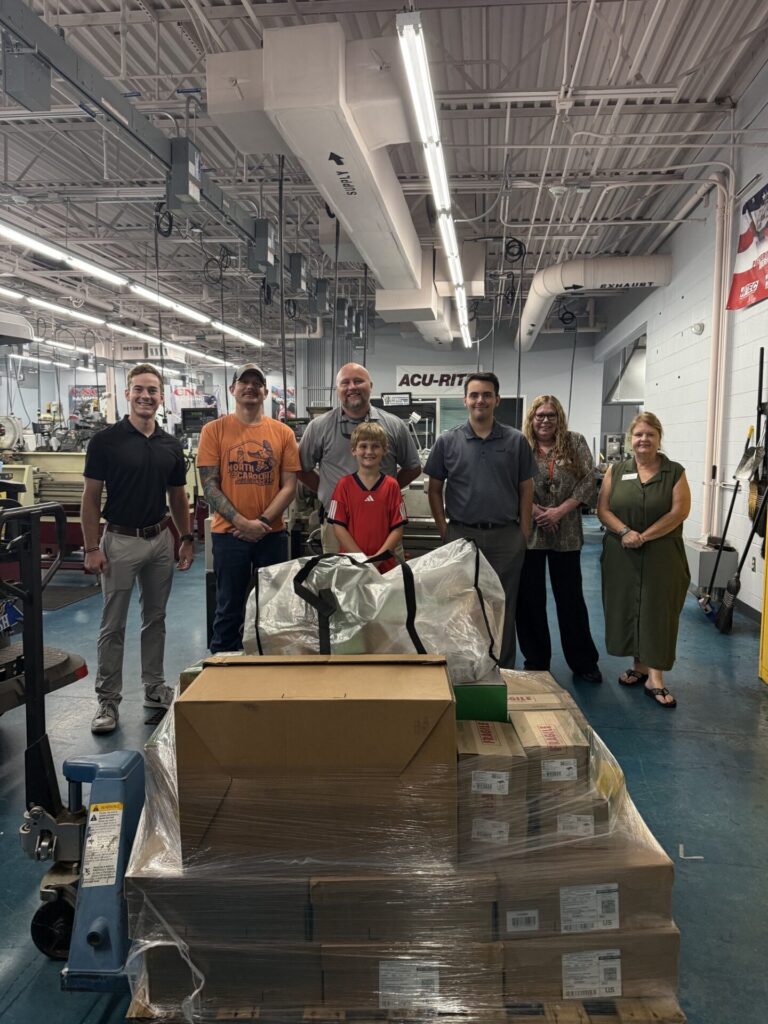 Photo of 6 adults and 1 child standing inside of a machining lab.